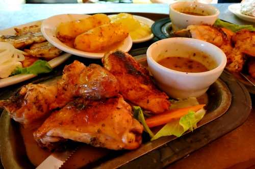 A platter of grilled chicken with sides of potatoes, sauce, and vegetables, served on a metal tray.