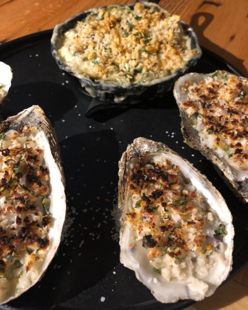 A plate of baked oysters topped with a golden breadcrumb mixture, garnished with herbs.