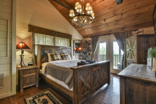 Cozy bedroom with wooden decor, a large bed, chandelier, and balcony doors leading to a scenic view.