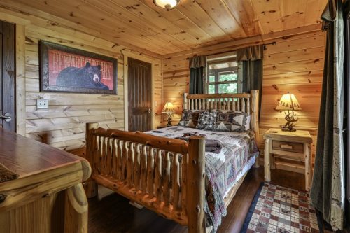 Cozy wooden bedroom with a log bed, quilted bedding, and rustic decor, featuring a bear painting and warm lighting.