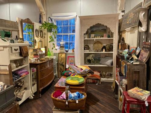 A cozy vintage shop filled with eclectic decor, furniture, and colorful textiles, illuminated by natural light.