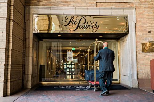 A bellhop pushes a luggage cart into the entrance of The Peabody hotel, showcasing its elegant facade.
