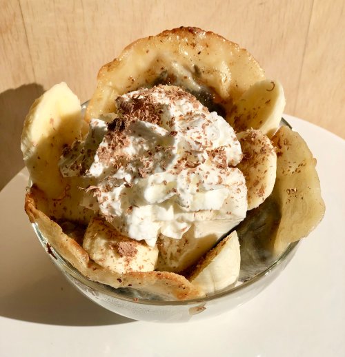 A glass bowl filled with banana slices, whipped cream, and chocolate shavings, all in a crispy dessert shell.