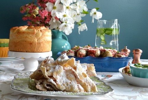 A colorful table setting featuring a dessert, a cake, a pitcher of infused water, and a platter of stuffed vegetables.