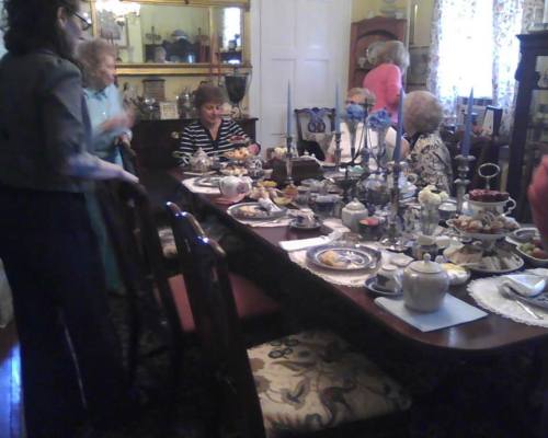 A group of women enjoying tea and pastries at a beautifully set dining table in a cozy room.