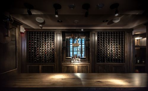 A dimly lit wine cellar featuring wooden racks filled with bottles and a central display on a wooden counter.