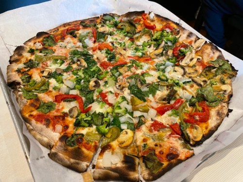 A freshly baked pizza topped with vegetables like bell peppers, onions, mushrooms, and herbs, with a crispy crust.
