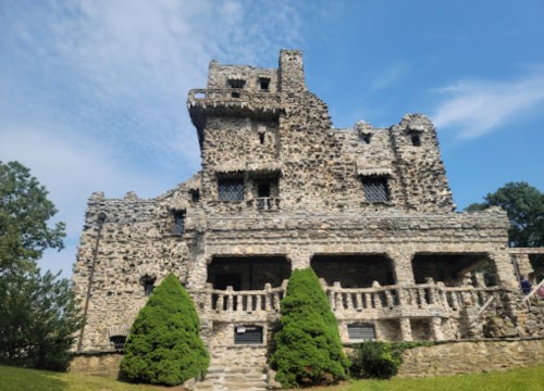 A stone castle with multiple levels, surrounded by greenery and a blue sky.