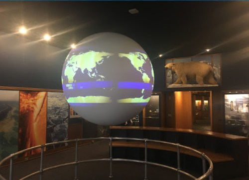 A large globe displaying a world map, surrounded by exhibit displays in a museum setting.