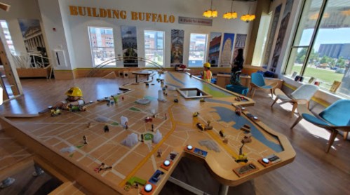 A large interactive map of Buffalo with toys and tools, featuring a person exploring the display in a bright room.
