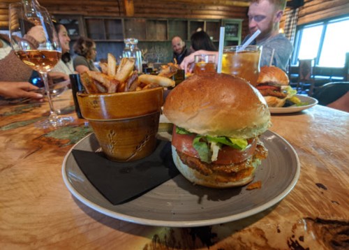 A plate with a burger topped with lettuce and tomato, alongside a cup of fries, in a rustic dining setting.
