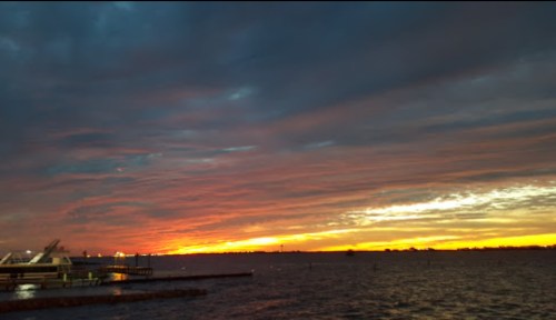A vibrant sunset over a calm body of water, with colorful clouds and silhouettes of a pier in the foreground.