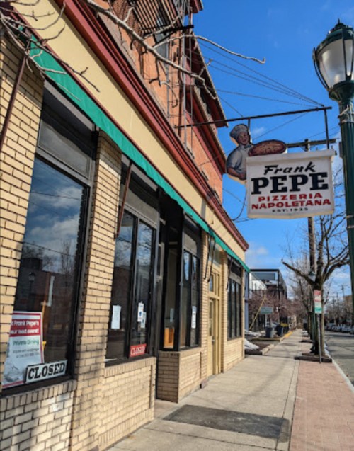 Exterior of Frank Pepe Pizzeria Napoletana, featuring a closed sign and a vintage hanging sign with a chef.