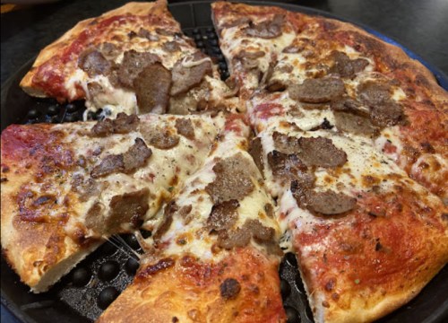 A close-up of a pizza topped with melted cheese and slices of meat on a black pizza pan.