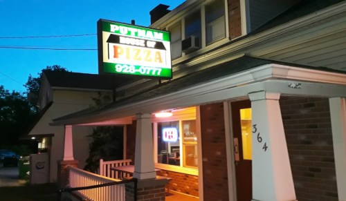 A pizza shop exterior at dusk, featuring a brightly lit sign that reads "Putnam House of Pizza."