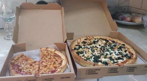 Two pizza boxes on a countertop: one with cheese and meat, the other topped with spinach and feta.