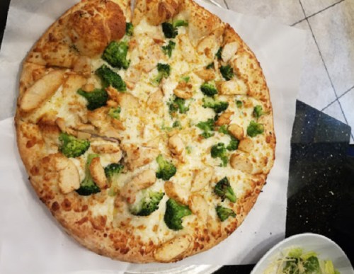A pizza topped with chicken, broccoli, and cheese on a golden crust, served with a side salad.