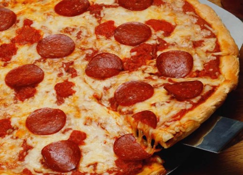 A close-up of a pepperoni pizza with melted cheese and a slice being pulled away, revealing gooey cheese underneath.