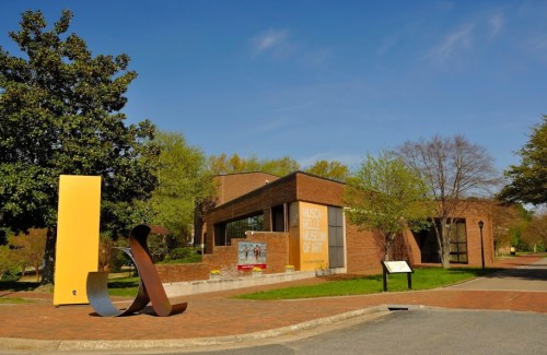 Exterior view of the Muscogee County Museum of Art, featuring modern sculptures and greenery under a clear blue sky.