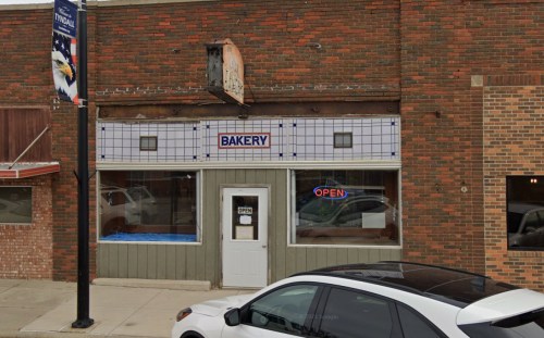 A small bakery storefront with a blue "OPEN" sign, featuring a brick exterior and large windows.