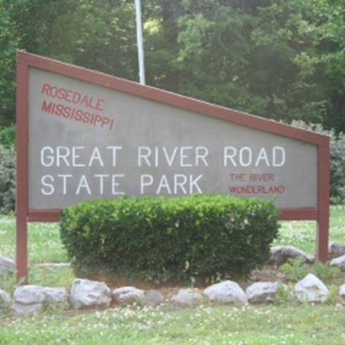 Sign for Great River Road State Park in Rosedale, Mississippi, surrounded by greenery and rocks.