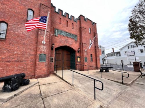 Historic brick building with an arched entrance, American flags, and cannons displayed outside.