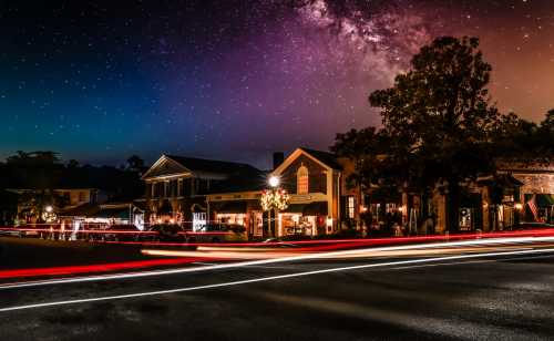 A charming street scene at night with shops, starry sky, and light trails from passing cars.