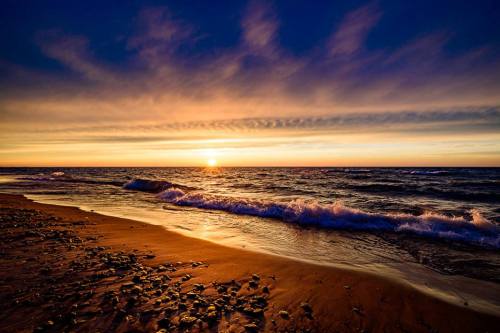 A serene beach at sunset, with gentle waves lapping at the shore and colorful clouds in the sky.
