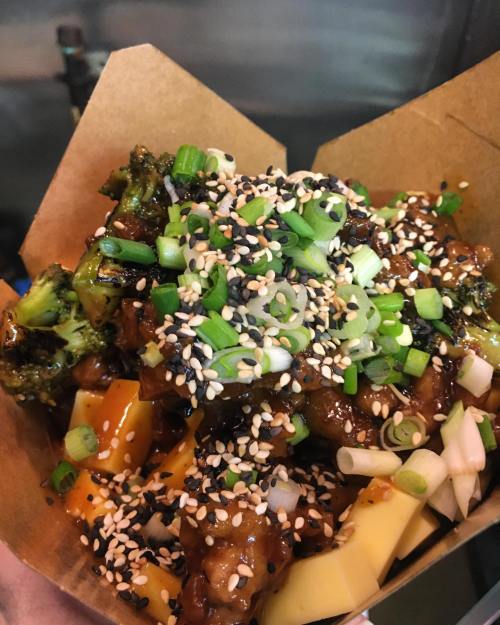A close-up of a dish featuring broccoli, colorful vegetables, sesame seeds, and green onions in a takeout container.