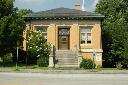 A historic yellow brick building with a staircase, surrounded by trees, under a clear blue sky.