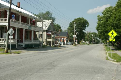 A quiet street scene featuring historic buildings, power lines, and a pedestrian crossing sign on a sunny day.
