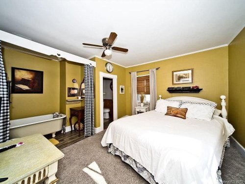 Cozy bedroom with a large bed, vintage decor, and a bathtub, featuring warm yellow walls and checkered curtains.