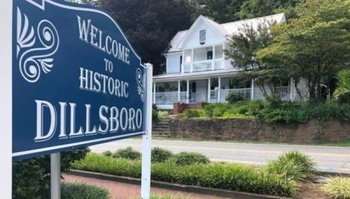 Sign reading "Welcome to Historic Dillsboro" in front of a white house surrounded by greenery.
