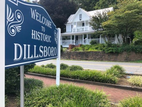 Sign welcoming visitors to historic Dillsboro, with a charming white house and greenery in the background.