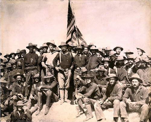 A historic group photo of soldiers, including Theodore Roosevelt, posing with an American flag during the Spanish-American War.
