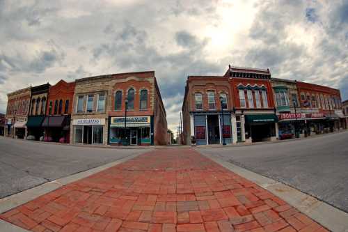 A wide view of a historic downtown street with brick pavement and vintage storefronts under a cloudy sky.