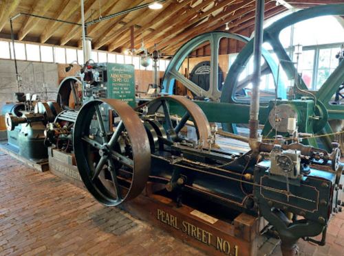 Historic machinery displayed in a spacious workshop, featuring large wheels and intricate mechanical components.