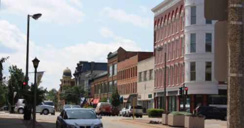 A street view featuring historic buildings, parked cars, and a clear blue sky.