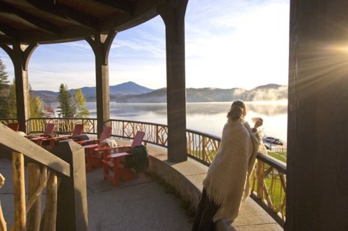 A person in a cozy sweater enjoys a serene lake view from a wooden balcony at sunrise.