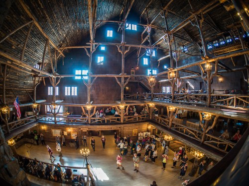 A spacious wooden hall with high ceilings, filled with people dancing and socializing under warm lighting.
