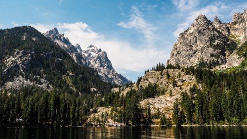 A serene mountain landscape with towering peaks, lush forests, and a calm lake reflecting the sky.
