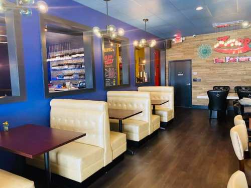 Interior of a restaurant featuring beige booths, dark tables, and blue walls with decorative lighting.