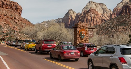 A long line of cars queuing at the entrance sign for Zion National Park in Utah.