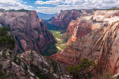 A breathtaking view of Zion Canyon, showcasing towering cliffs and a winding river below under a partly cloudy sky.
