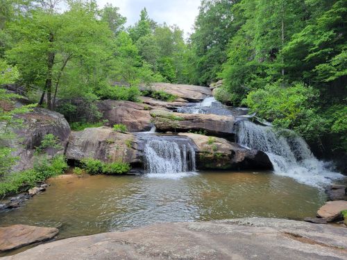 A serene waterfall cascading over rocky ledges, surrounded by lush green trees and a calm pool of water below.
