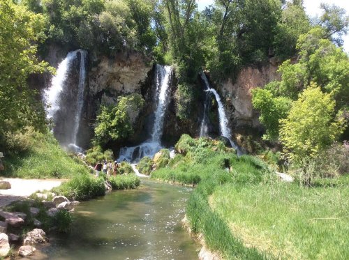 A serene landscape featuring multiple waterfalls cascading into a lush green area with a flowing river.