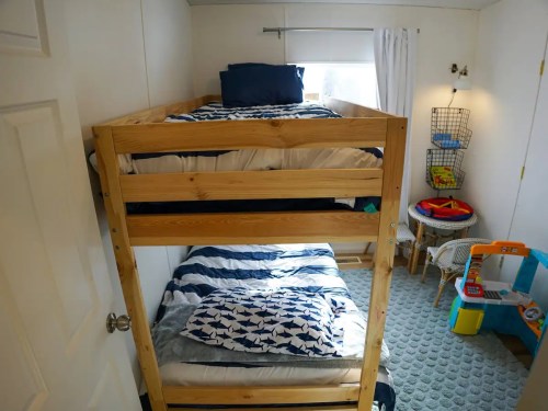A cozy bedroom featuring a wooden bunk bed with blue and white bedding, a play area, and a window with curtains.