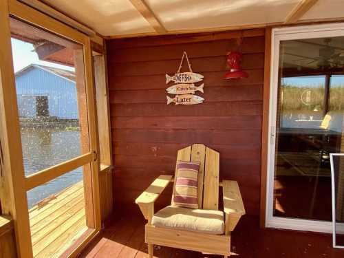 A cozy wooden chair on a porch with a fishing-themed sign and a view of water outside.