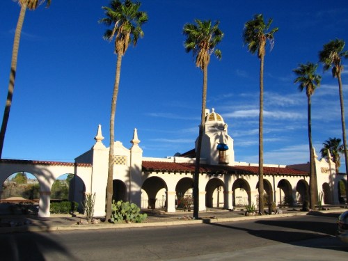 A historic building with arched windows and a dome, surrounded by palm trees against a clear blue sky.