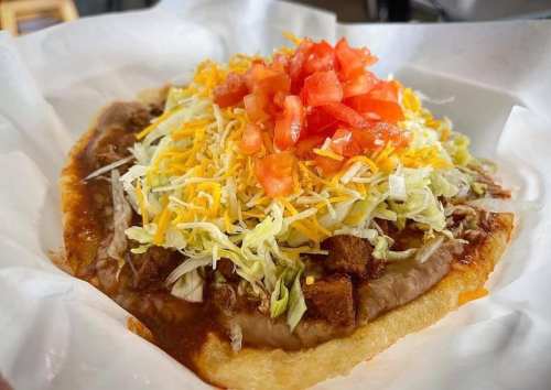 A close-up of a taco topped with lettuce, cheese, diced tomatoes, and refried beans on a crispy shell.